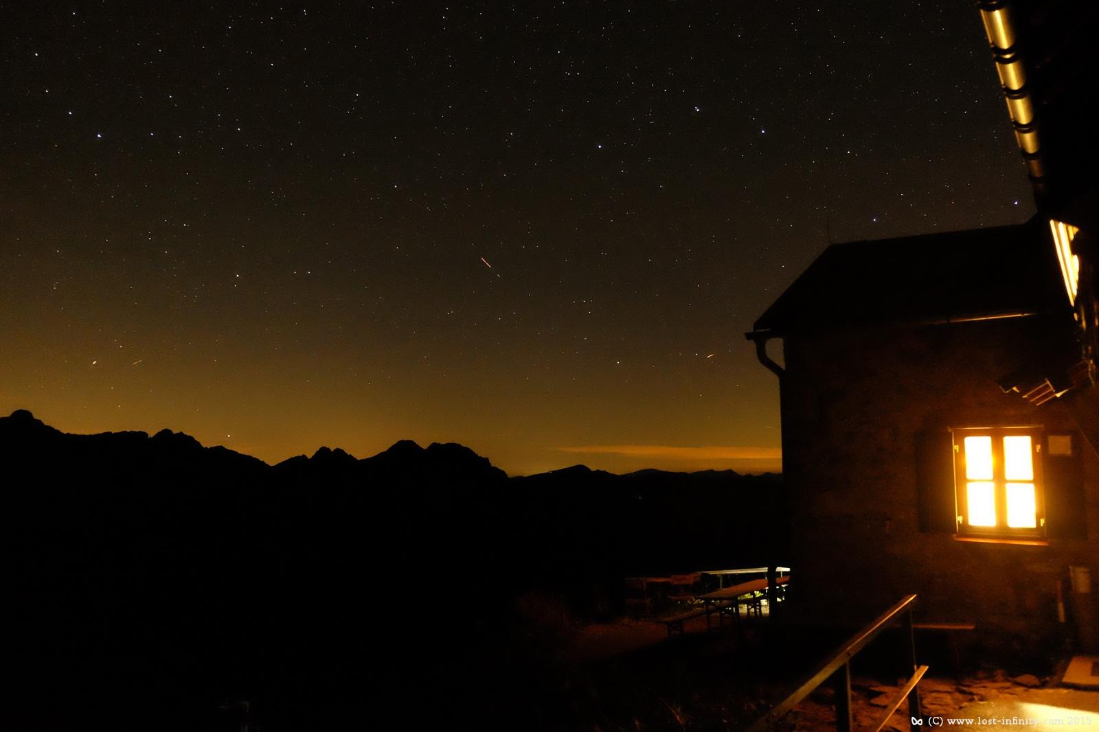 Illuminated mountain hut in front of mountains and night sky